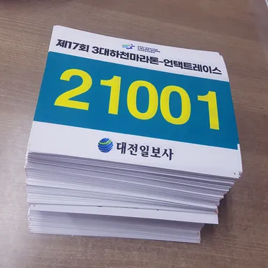 대회명과 번호가 인쇄된 마라톤 배번표가 여러 장 쌓여 있는 실제 사진